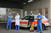 Drei Ärzte und eine Notärztin neben dem Notarztwagen vor der Liegendanfahrt für Rettungswagen im Krankenhaus Dernbach